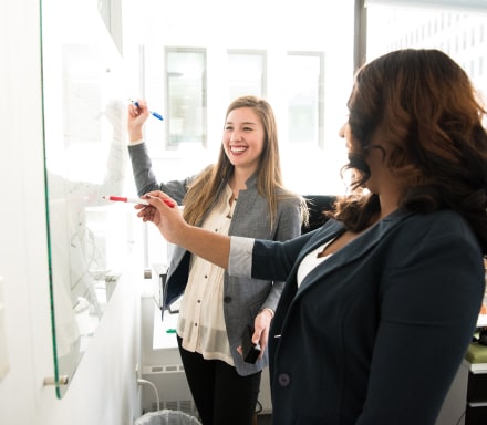 two womans analyzing a whiteboard data